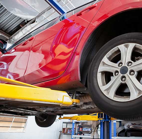 NCC Red car lifted on hydraulic car lift in a workshop during routine service