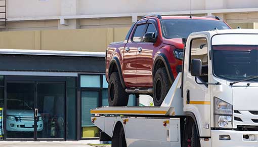 NCC red pickup car loaded onto white towing truck in public area for transportation to garage